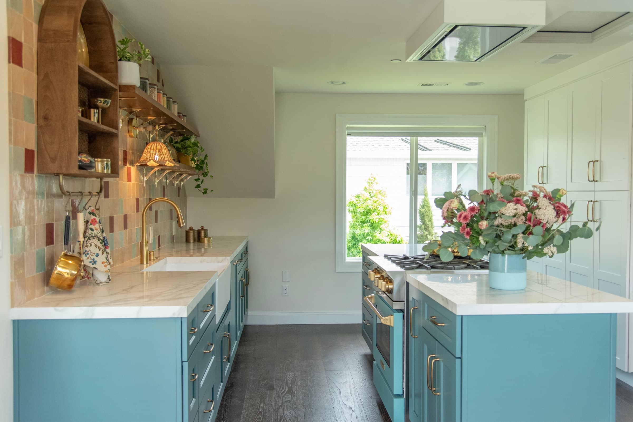 Renovated kitchen with teal cabinetry, brass fixtures, and a marble island