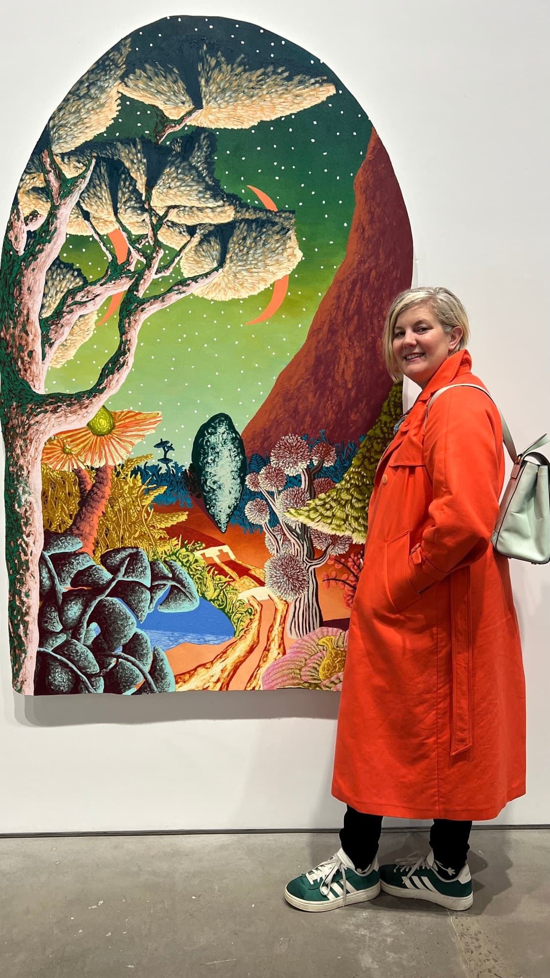 Skye Howell Henley standing beside a large colorful landscape painting